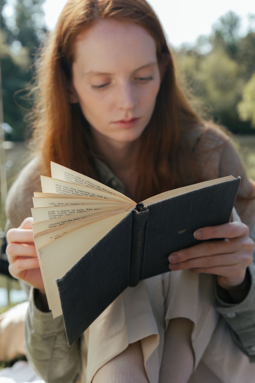 A woman peacefully reading a book in a park, finding calm away from the noise