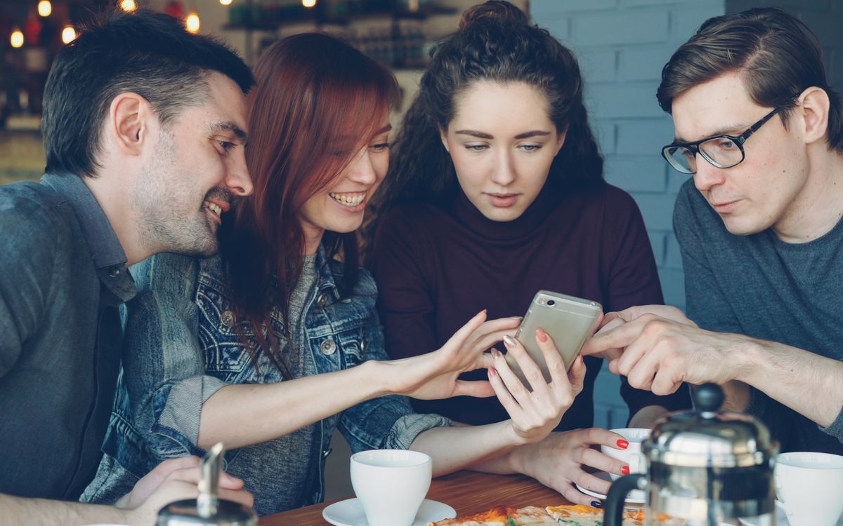 Friends sharing coffee and scrolling their phones together, the kind of togetherness a group chat cannot replace