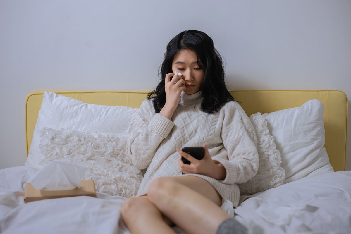 Woman sitting alone on a bed looking sadly at her phone after being left on read