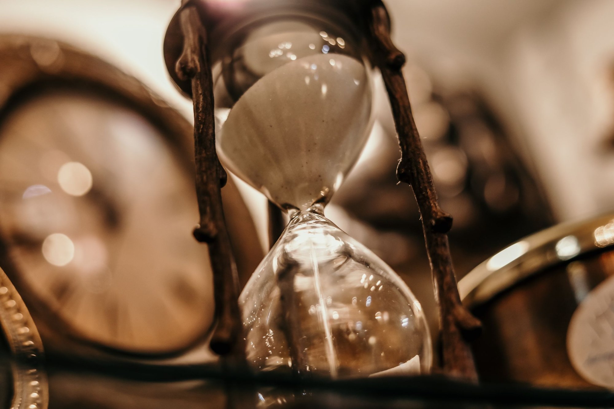 An hourglass with sand running out beside a blurred antique clock, the minutes a late arrival spends without asking