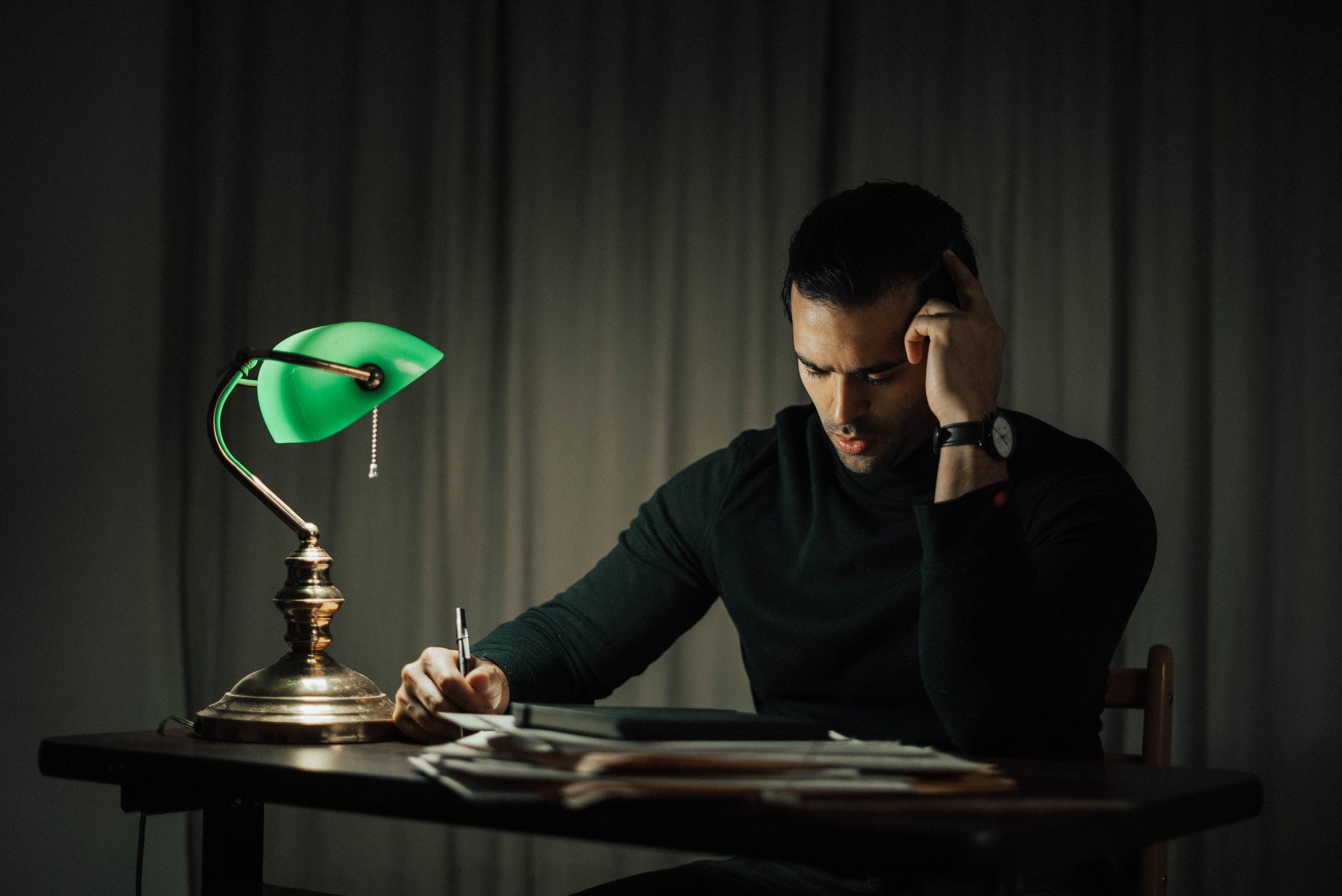 A man writing thoughtfully at his desk by lamplight, the embodied human thinking a machine can imitate but never share