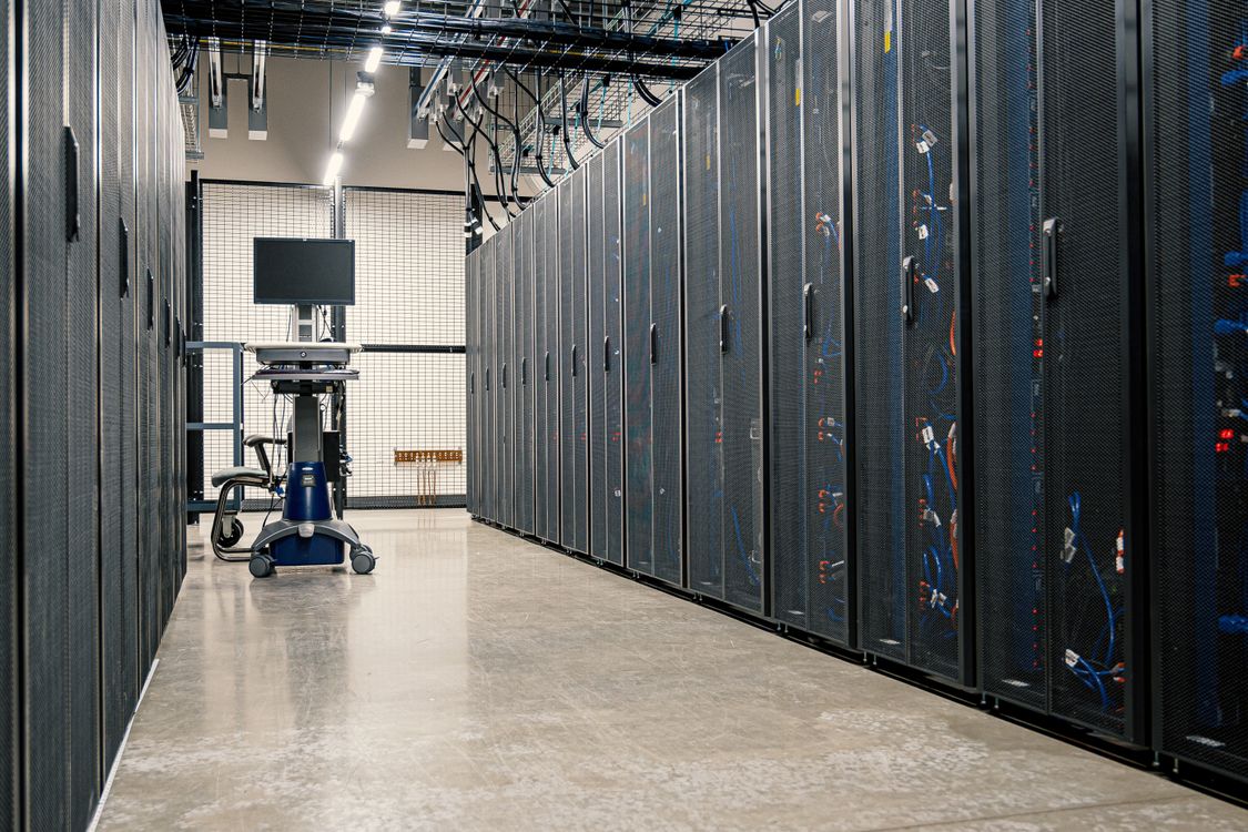 Rows of black server racks along a brightly lit aisle in a data center