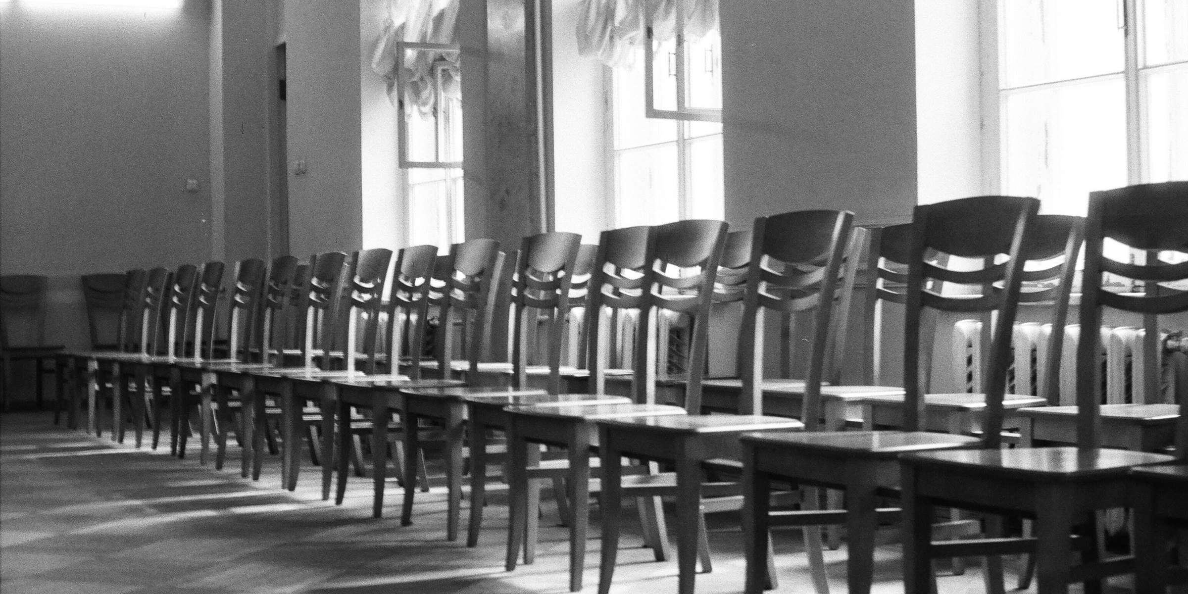 Rows of empty wooden chairs in a sunlit room, seats left vacant