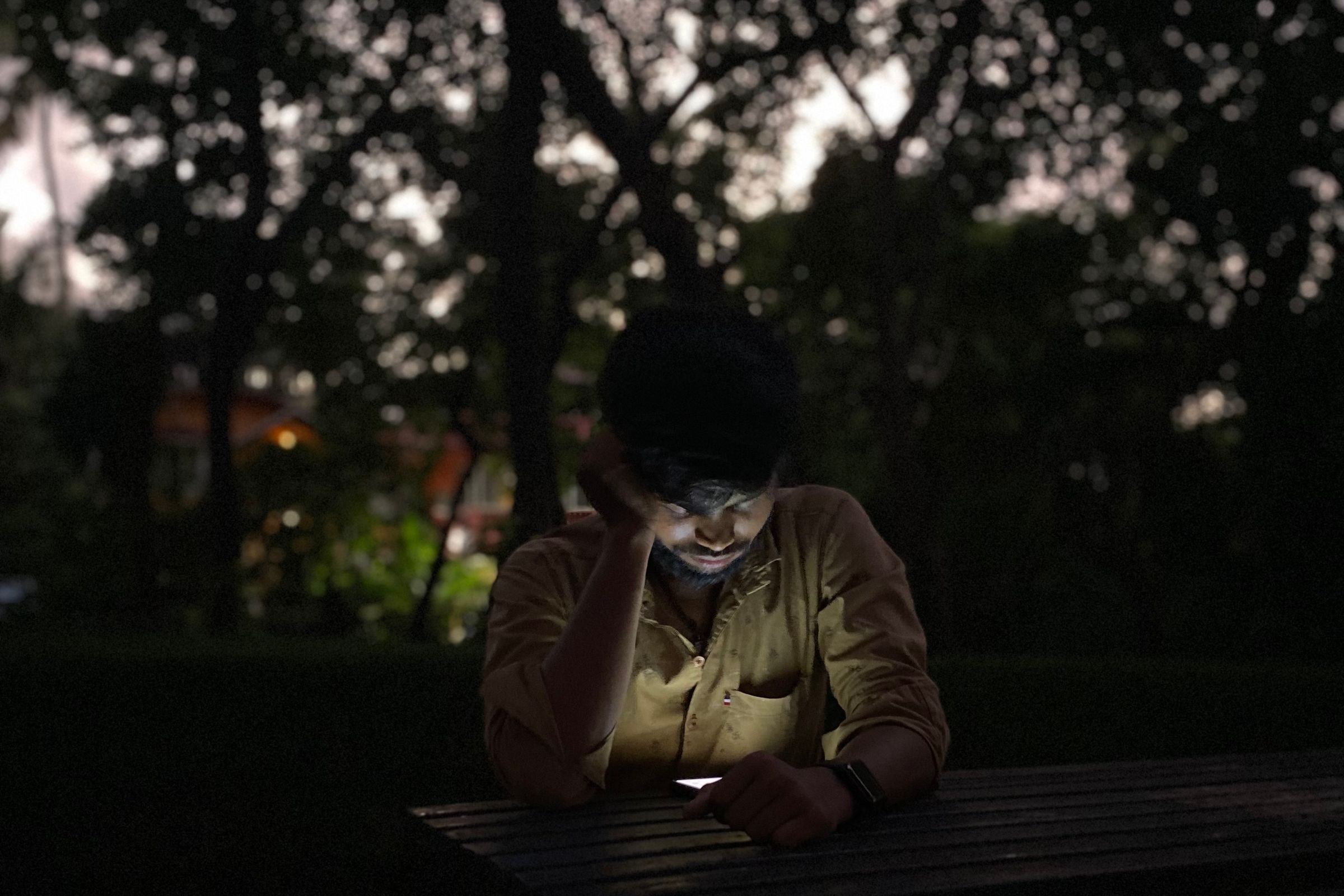 The Friend Who Cannot Disagree: On AI Chatbots, Delusion, and the Cost of Being Believed 3 A man sitting alone at a picnic table after dark, his face lit from below by his phone screen