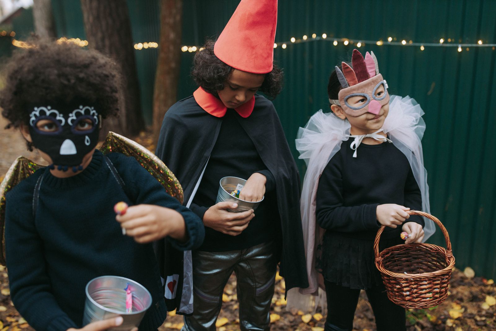 Three children in Halloween costumes collecting candy while trick-or-treating