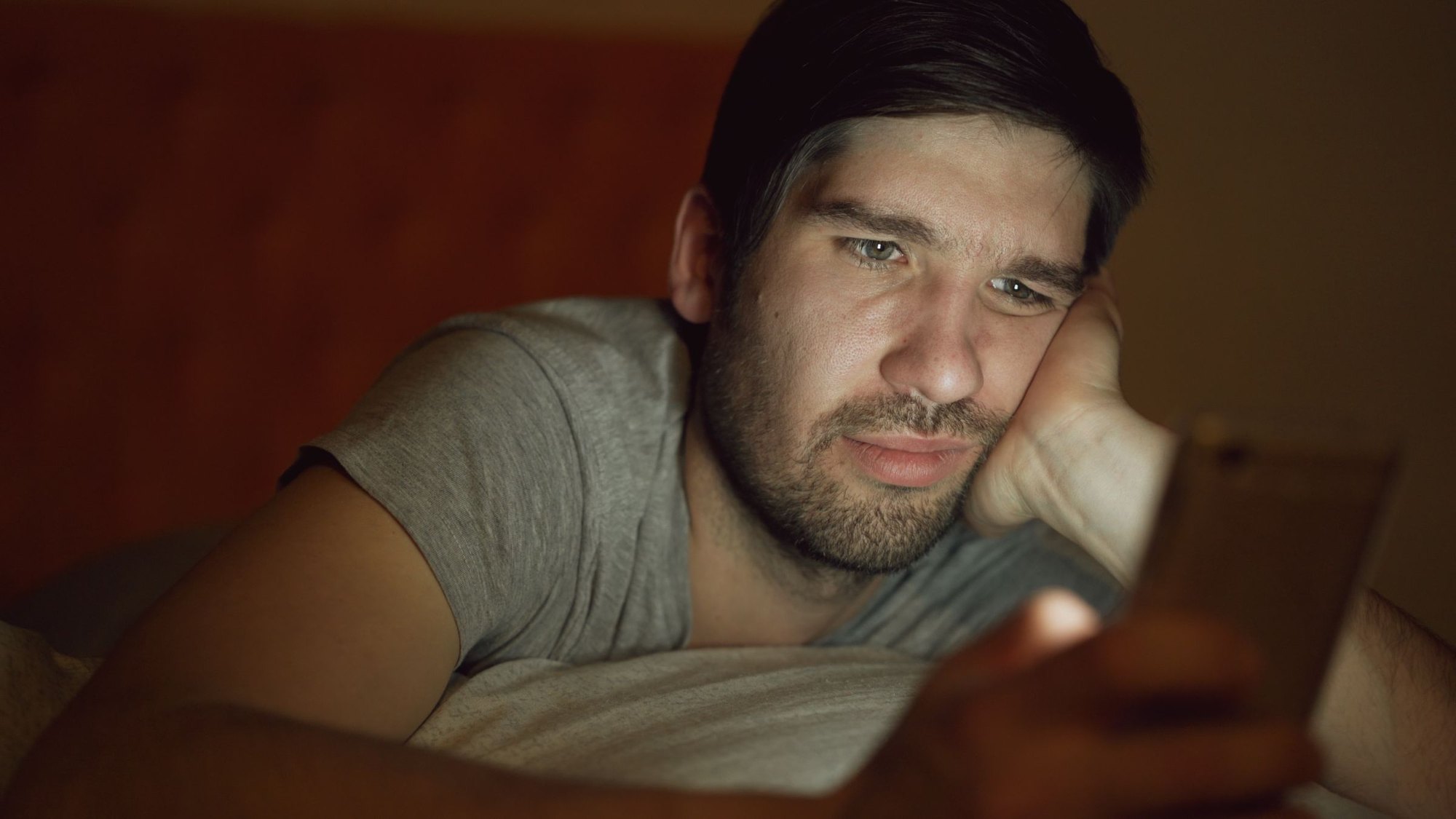A man sitting alone in a dim room, looking at his phone at night